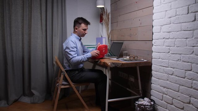 Man experiences headache and opens a personal first aid kit, taking medication while working remotely on a laptop in a cozy home office setup, prioritizing his health