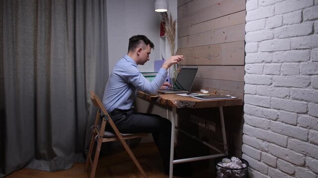 Man in casual clothes sits at a wooden desk in a home office, distracted and bored, twirling car keys while a laptop waitsremote worker procrastinating on tasks