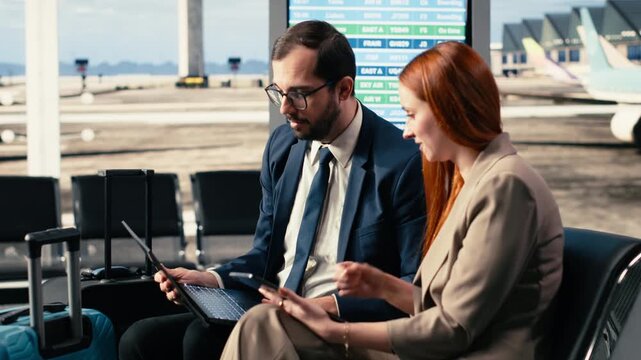Business colleagues working near departure gate at an airport terminal, reviewing itinerary and boarding pass while waiting for airplane. CEO and consultant coordinating plans for business trip.