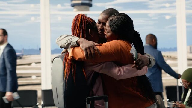 Emotional scene of African American parents hugging daughter in airport terminal, saying a bittersweet goodbye before departure flight. Young traveler leaving to study abroad, solo travel.