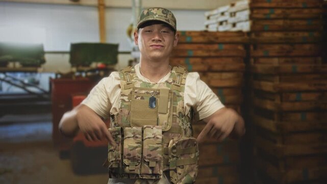 Man in military uniform points to tactical vest pouches inside a warehouse building; confidence duty.