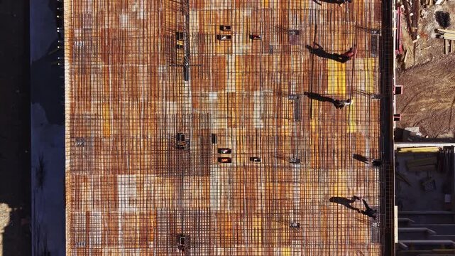 Several workers are seen organizing materials and setting up a construction site. The scene shows a large area of rebar laid out for a concrete pour.