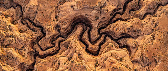 Obraz premium Vertical aerial of sculpted desert sandstone carved into swirling ravines and tight channels, revealing an intricate maze of eroded rock textures, warm earth tones, and abstract geology
