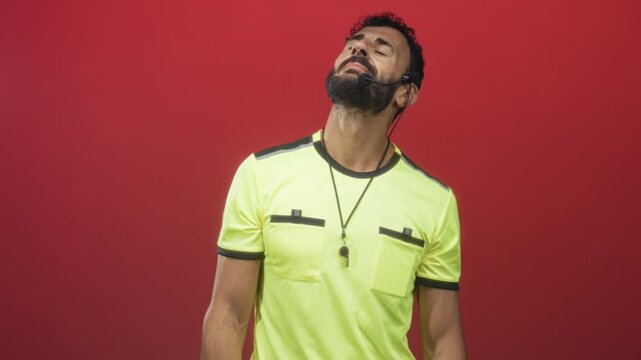 Man referee wearing neon shirt and whistle around neck tilts head back and closes eyes while headset mic rests at cheek in studio; exhaustion duty.