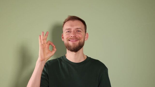 Happy man showing ok gesture and winking on light green background