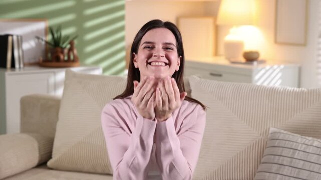 Smiling woman looking at camera and waving goodbye on sofa at home