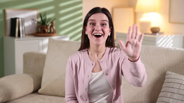 Smiling woman waving hello on sofa at home
