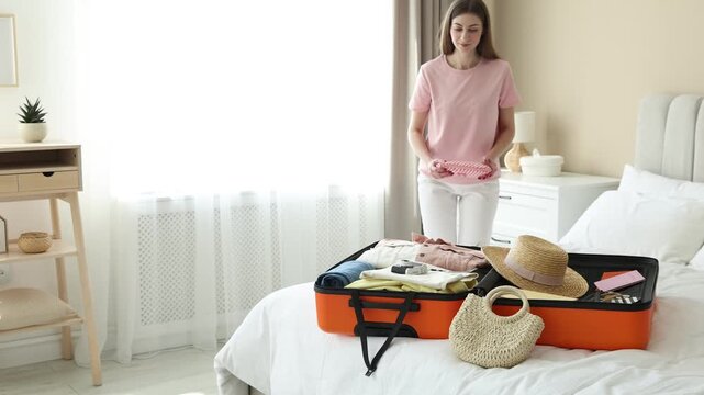 Beautiful woman packing her belongings into suitcase in bedroom