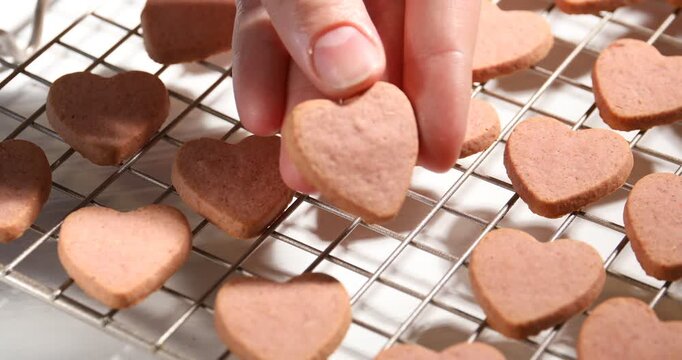 Woman taking tasty heart shaped oatmeal cookie from cooling rack at white table, closeup