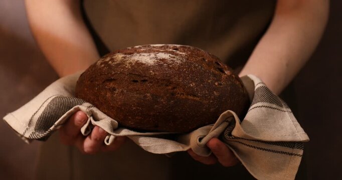 Woman holding loaf of fresh rye bread on brown background, closeup