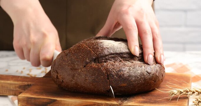 Woman cutting fresh bread at at table, closeup