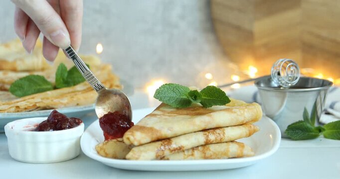 Woman pouring honey onto tasty crepes at white table, closeup