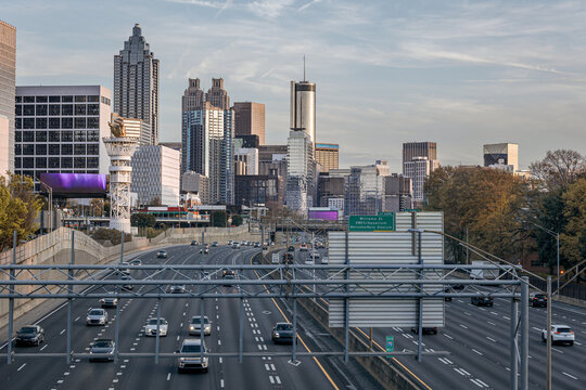 View of the Downtown Atlanta Skyline Cityscape showing several prominent buildings, highways, cars, and hotels on a beautiful clear evening as seen from a city street.
