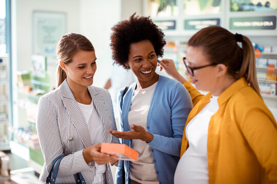 Pregnant woman with friends choosing medicine in pharmacy