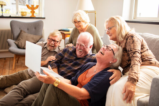 Happy senior friends laughing over laptop at home