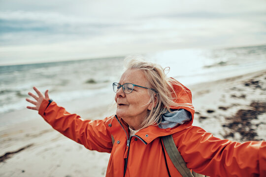 Senior woman with arms outstretched on windy beach