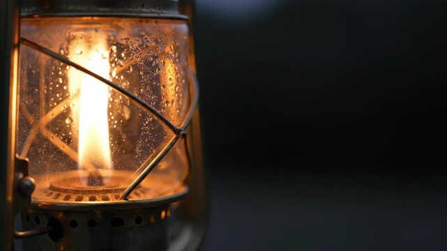 Close-up macro shot of an old-fashioned kerosene lantern with a lit flame, casting a warm glow in the darkness