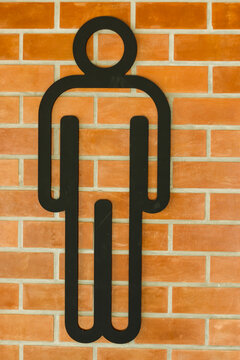 Men's restroom sign mounted on a warm orange brick wall.