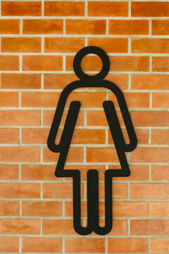 Women's restroom sign mounted on a warm orange brick wall.