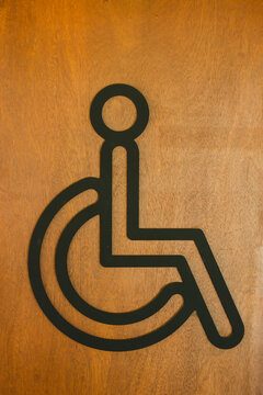 A wheelchair accessible sign is mounted on a light brown wooden surface.
