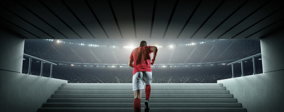 Rear view of a football player walking out of the tunnel onto the pitch. An imaginary soccer stadium is modelled and rendered.