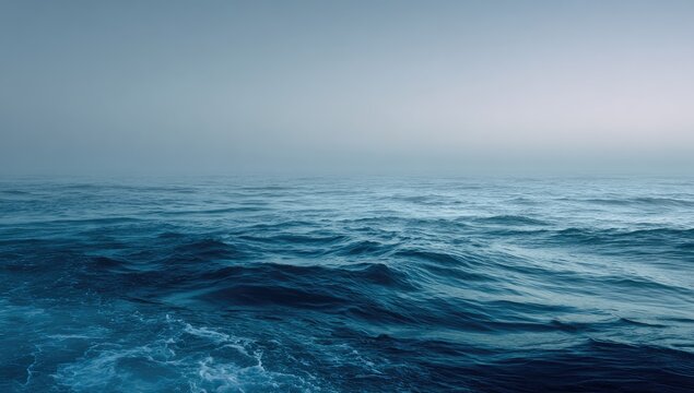 Moody shot of ocean waves under a hazy, overcast sky. Watery depths meet a misty horizon