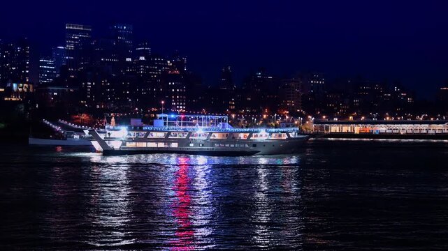 Illuminated sightseeing boat on East River at night New York. Sightseeing cruise ship with blue lights sailing on river with city skyline background at night.