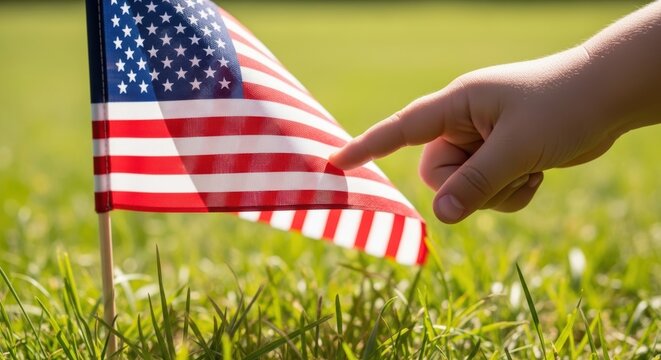 Child hand touching American flag in grass for Memorial Day