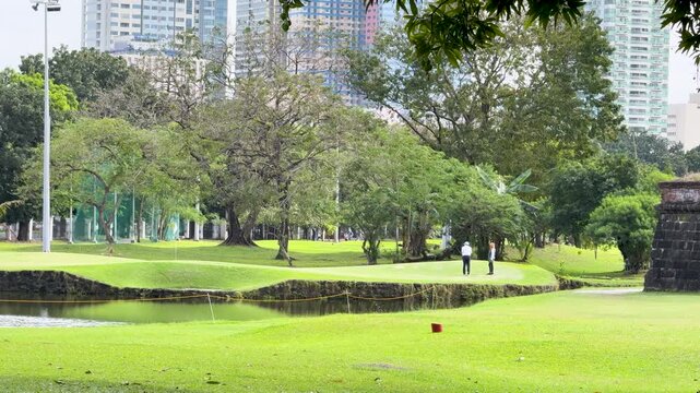 Golfers Playing on a Lush Green Course Near Manila City Skyline