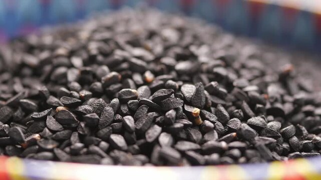 Macro view of black cumin seeds rotating slowly in colorful ceramic bowl with shallow depth of field.