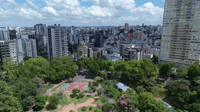 Parque Municipal Get&uacute;lio Vargas aerial flight rising over dense greenery, park paths and urban skyline in Caxias do Sul.