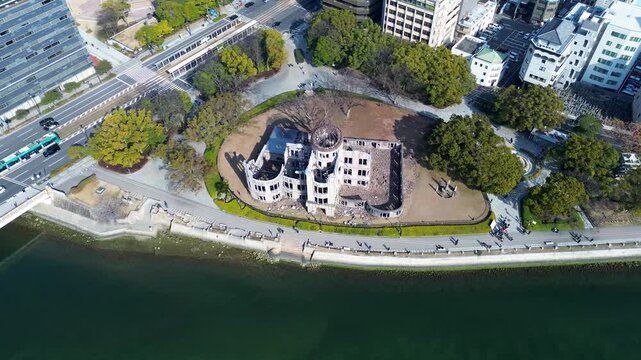 Drone aerial landscape of the historic Atomic Genbaku Dome structure landmark next to Motoyasu River with ferry boat and urban city buildings in background Hiroshima Peace Park Memorial Japan tourism
