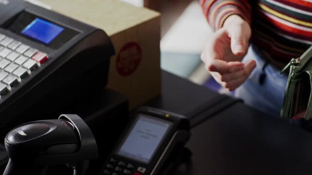 Rude, dismissive cashier begrudgingly takes cash from customer at register, creating awkward comedic tension during a retail transaction &mdash; close-up shot