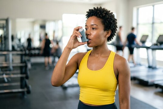 A young black woman inhales asthma medicine in the gym. Bronchial asthma, COPD, metered-dose inhaler, sports, fitness, healthy lifestyle.