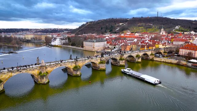 Aerial panorama of Charles Bridge crossing the Vltava in Prague with iconic rooftops and towers under cloudy weather; perfect for tourism marketing, travel guides and architecture editorials