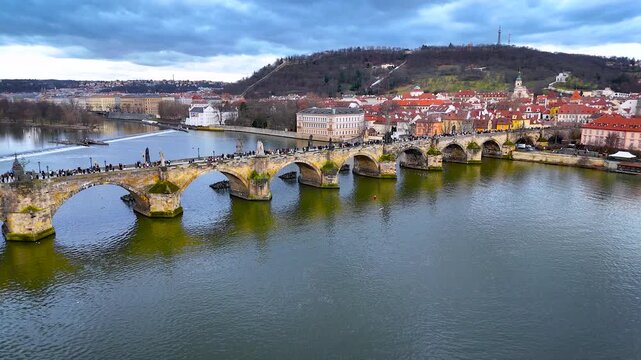 Aerial panorama of Charles Bridge crossing the Vltava in Prague with iconic rooftops and towers under cloudy weather; perfect for tourism marketing, travel guides and architecture editorials