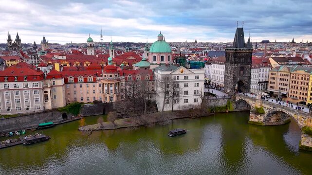 Aerial panorama of Charles Bridge crossing the Vltava in Prague with iconic rooftops and towers under cloudy weather; perfect for tourism marketing, travel guides and architecture editorials