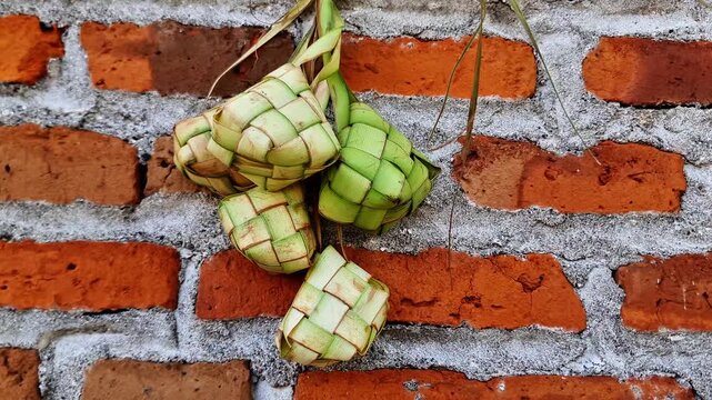 Traditional Indonesian Ketupat  Hand Woven Rice Cakes Hanging on Rustic Red Brick Wall for Eid Celebration