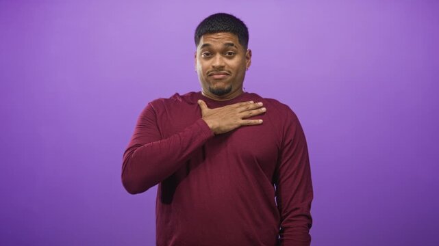 Man with hand on chest and slight shrug in studio purple backdrop, wearing burgundy long sleeve shirt and small earring; apologetic.