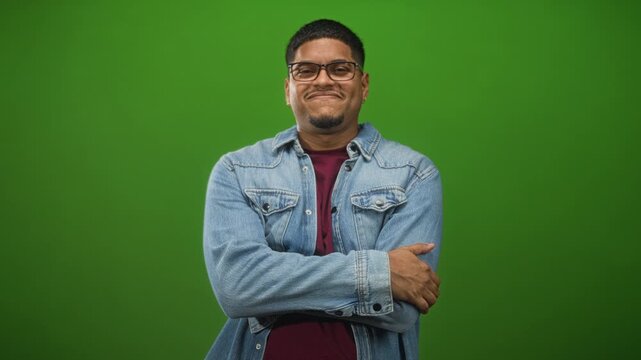 Man with folded arms and hand on elbow wearing glasses and denim jacket in studio; calm confidence approachable.