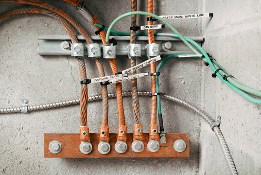 Electrical grounding and bonding busbar system in electrical room.  Labeled grounding rods. Copper conductors, clamps, and grounding electrodes mounted on wall. Selective focus.
