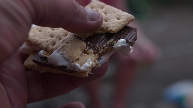 Close up of person holding messy s'more with melting chocolate and marshmallow on graham cracker