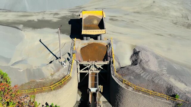 Dump truck positioned above gravel hopper and conveyor system at quarry
