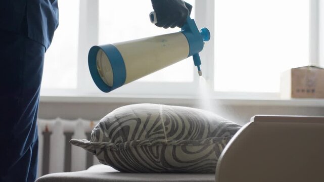 White Male Technician Fogging Cushion Cleaning Bright Window Backdrop Handheld Pump Sprayer Releasing Dense Mist Over Patterned Cushion Protective Gloves Focus On Mist Particles Residential Sanitizing