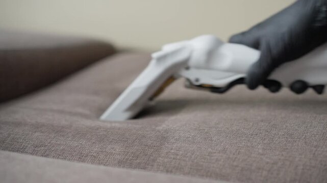 Detailed Cleaning Process. Professional Cleaner Targeting Sofa Stain Precisely Today. Caucasian Cleaner Employs Handheld Device For Accurate Stain Removal Along Sofa Seams Effectively