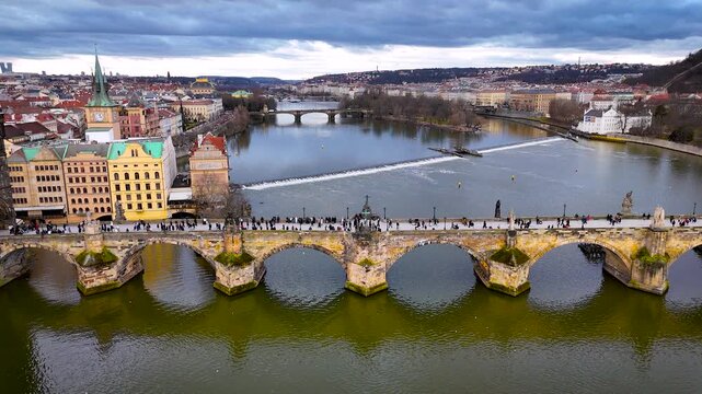 Aerial panorama of Charles Bridge crossing the Vltava in Prague with iconic rooftops and towers under cloudy weather; perfect for tourism marketing, travel guides and architecture editorials