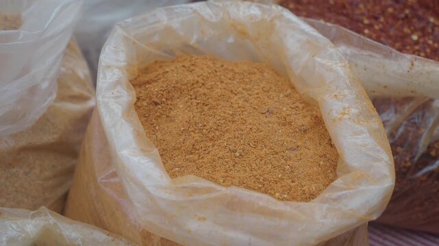 Ground cumin and dried chili flakes in plastic bags at outdoor market stall.