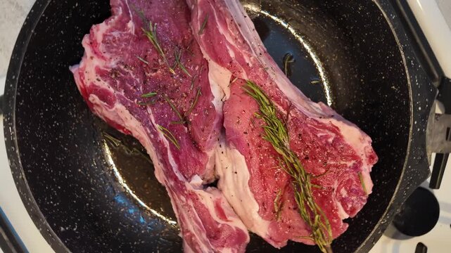 Raw tomahawk beef steak with rosemary and pepper cooking in hot frying pan top view kitchen footage.