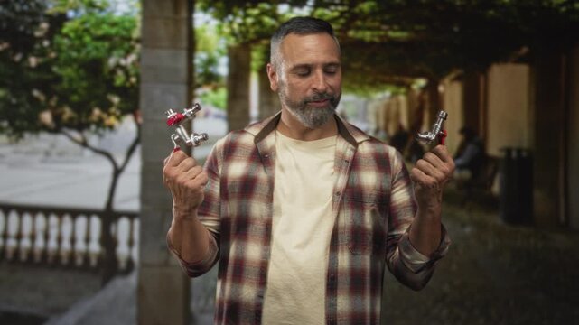 Man middle age hispanic with gray hair and beard smiling while holding two faucets in both hands on street; pride repair craftsmanship.