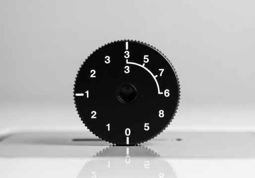 Close-up of a black rotary dial with white numbers, including negative values and a curved indicator, isolated on a light gray reflective surface, symbolizing adjustment and measurement.
